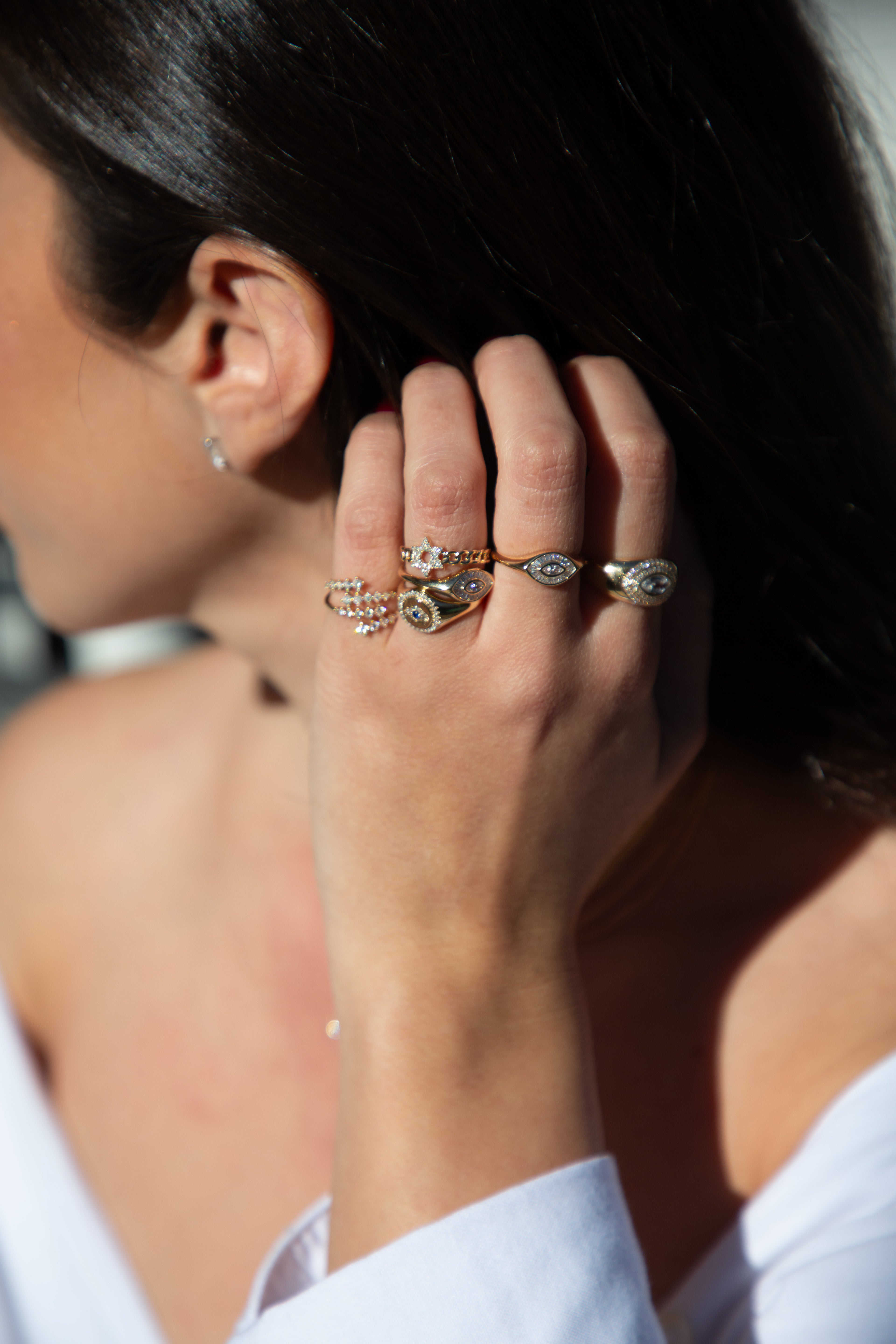A person's hand showcasing a gold ring with a marquise-cut diamond centered in a halo of baguettes on a white shirt sleeve background.