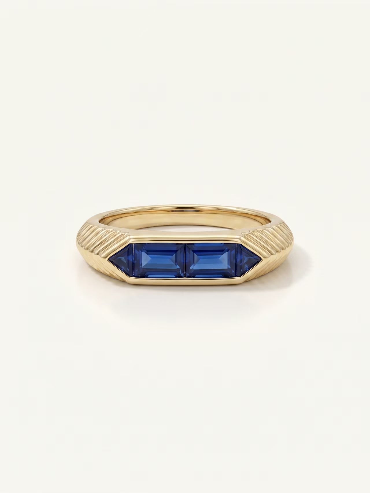 A gold signet ring featuring two rectangular blue gemstones, photographed on a clean, light off-white background.